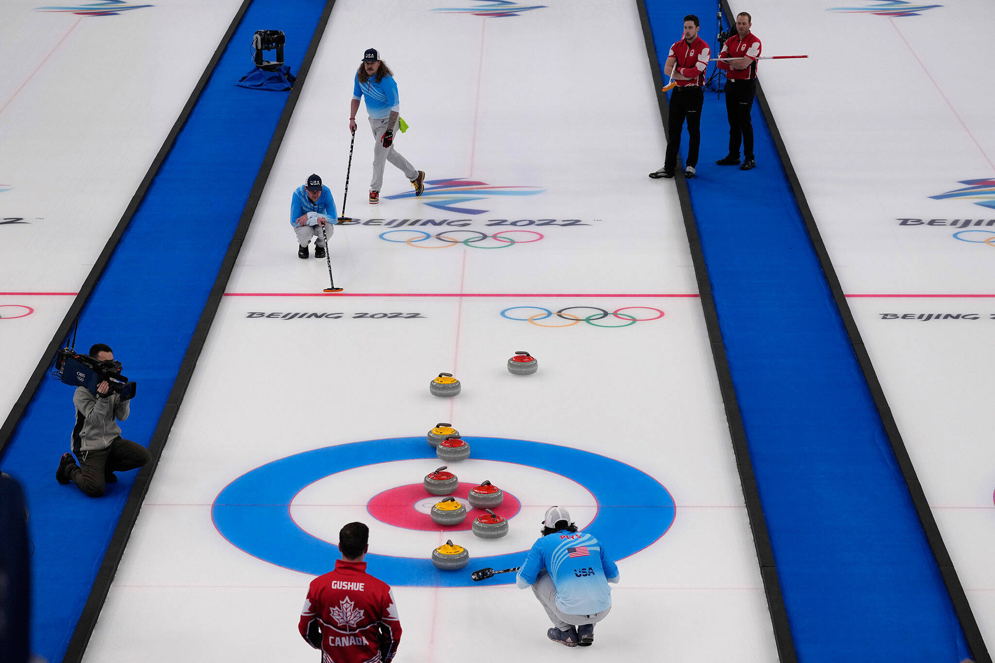 Players watch a rock approach the button during the men’s curling bronze-medal match between Canada and the United States on Friday at the Winter Olympics in Beijing. (AP Photo/Nariman El-Mofty)