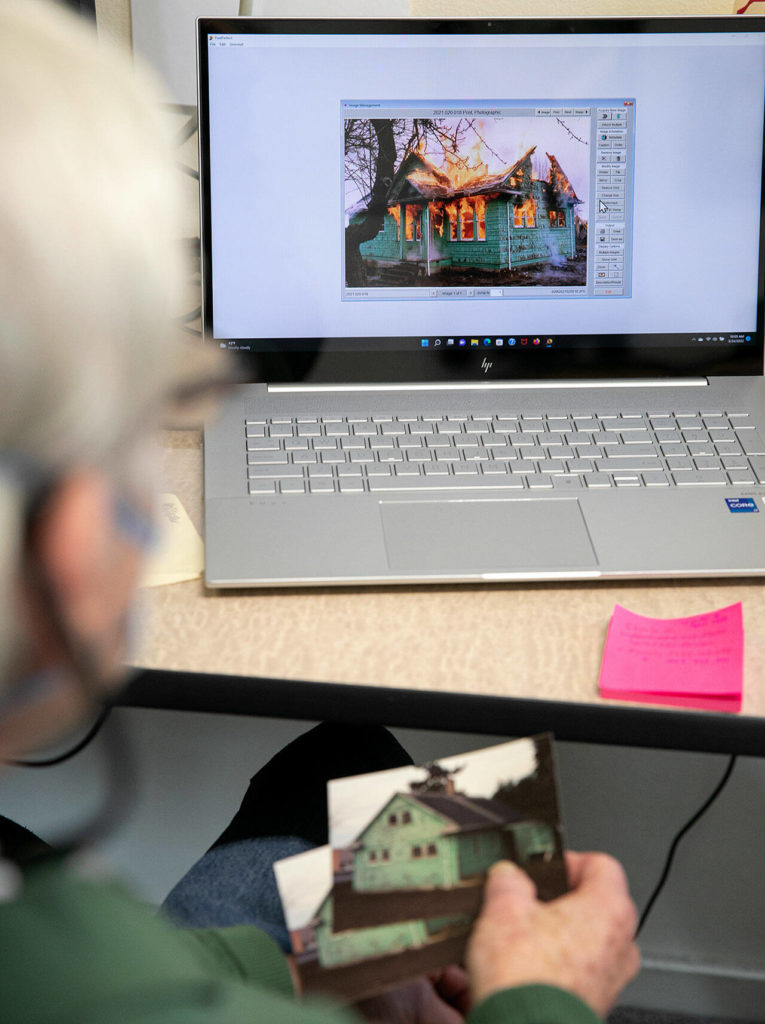 Peter Anderson holds photos of an old Mukilteo home while displaying images on his computer from the time the home was intentionally burned down by the fire department in the 1990s. (Ryan Berry / The Herald)
