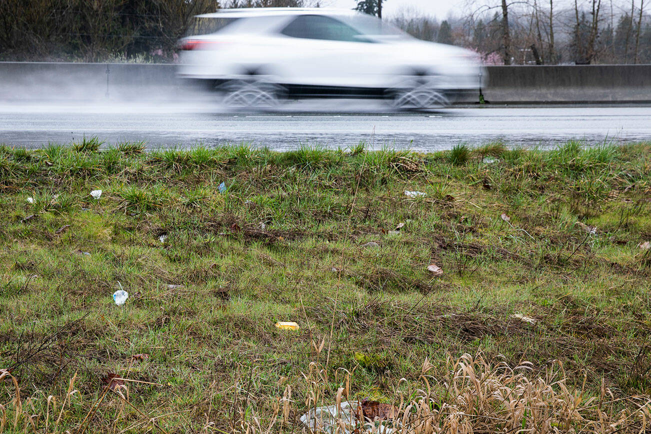 Pieces of trash litter the side of Highway 522 as a car drives by on Monday, March 21, 2022 in Monroe, Washington. (Olivia Vanni / The Herald)