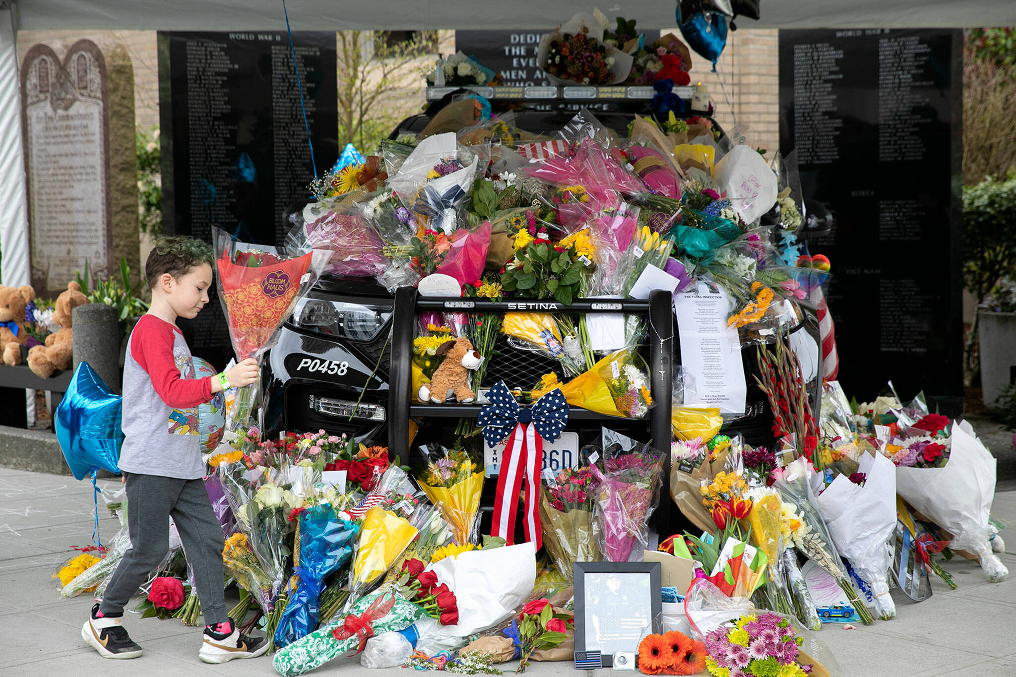 A young child brings flowers to the memorial of fallen Everett Police Officer Dan Rocha on Saturday in Everett. (Ryan Berry / The Herald)