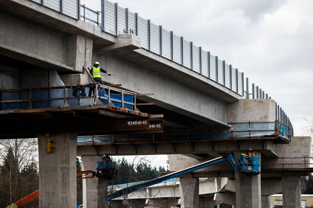 Construction workers walk along the underside of the Lynnwood Link light rail tracks on Tuesday, March 29, 2022 in Lynnwood, Washington. (Olivia Vanni / The Herald)