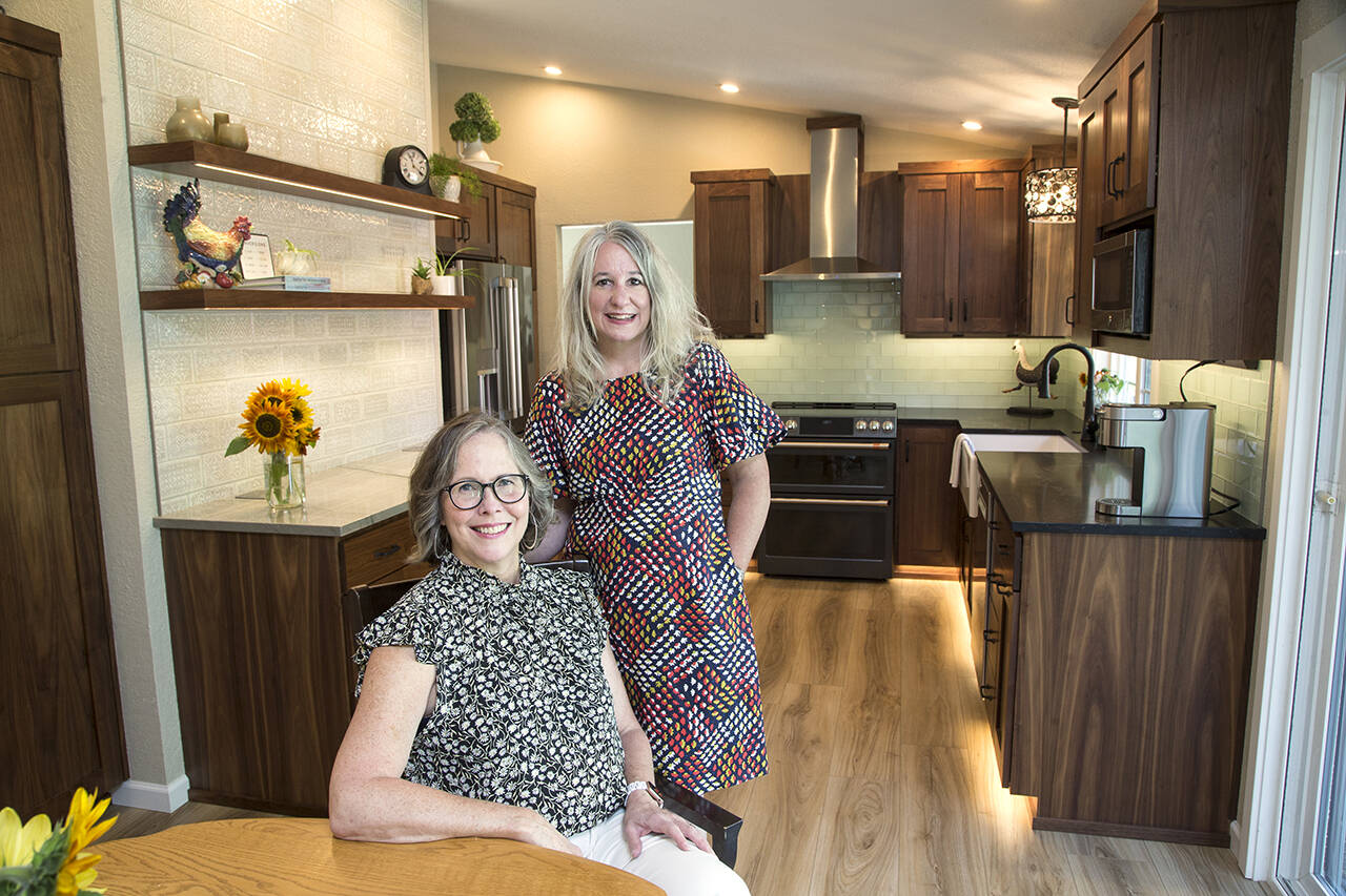 Mary Beth Kurtenbach sits in her remodeled kitchen, designed by Lake Stevens’ Distinctive Interior Designs’ Kelly DuByne (right) in Lake Stevens. The kitchen features a Monet-inspired tile wall, floating shelves and toe kick lights. (Andy Bronson)