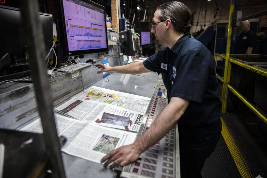 Alex Hanson looks over sections of The Daily Herald and adjusts the ink at the plant at Paine Field in Everett. (Olivia Vanni / The Herald)
