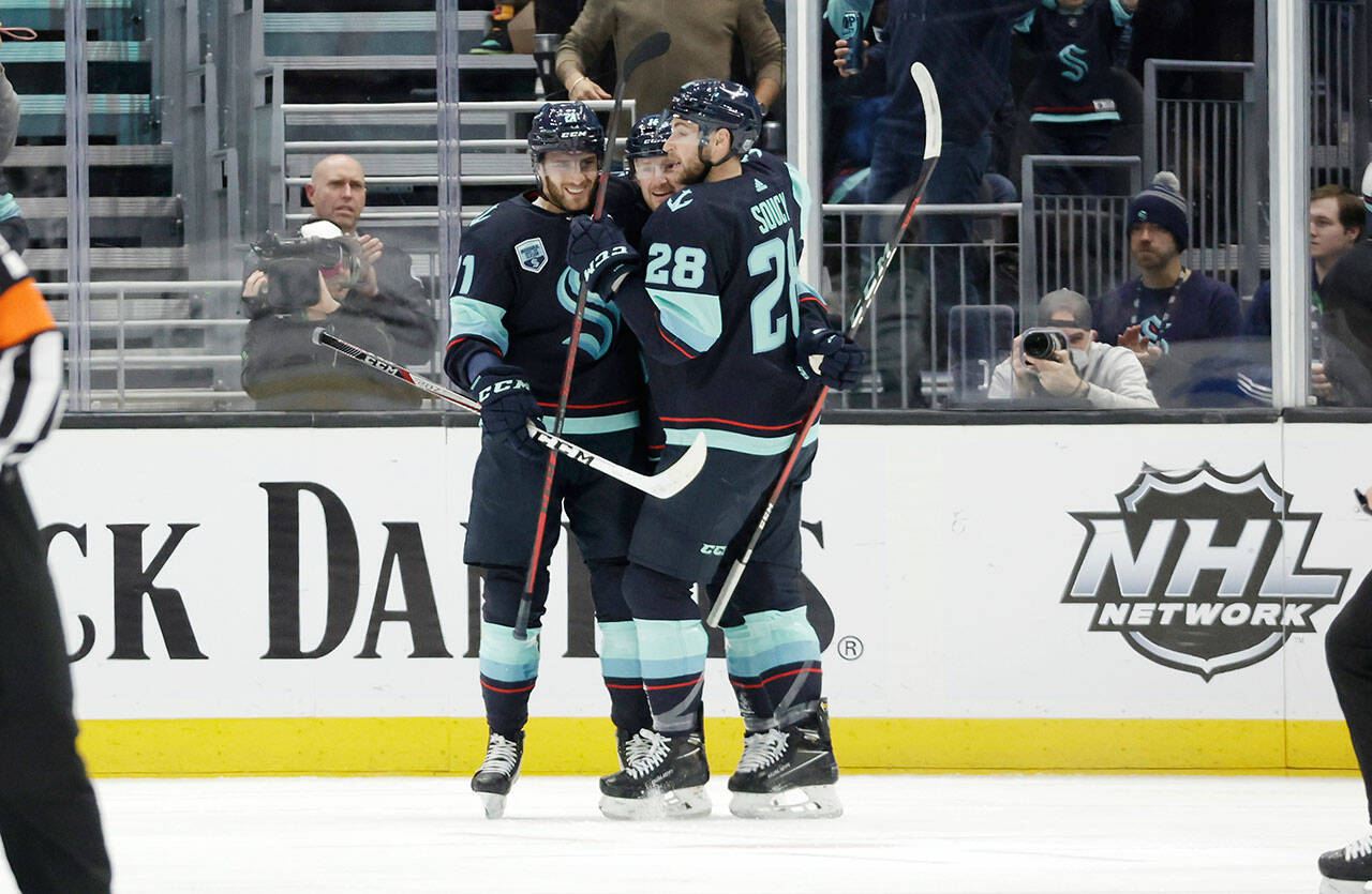Seattle Kraken center Alex Wennberg (left) and defenseman Carson Soucy (28) embrace left wing Jared McCann after he scored against the Dallas Stars during a game Sunday in Seattle. (AP Photo/John Froschauer)