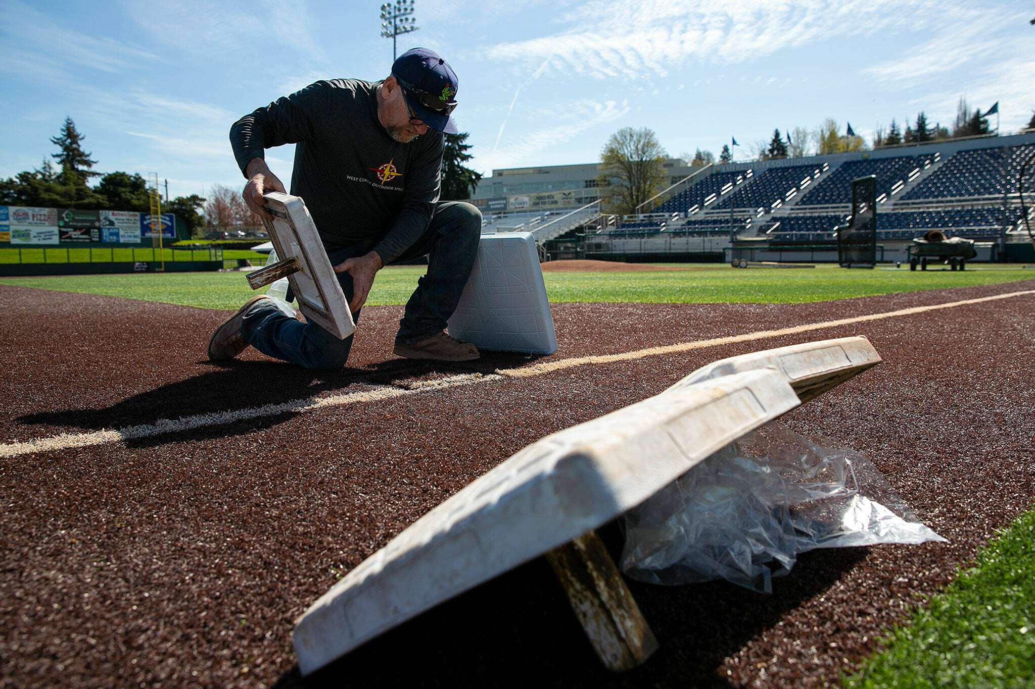 AquaSox head groundskeeper Ken Brooks changes out third base to one of the new larger bases being used in the minors prior to a team workout Wednesday at Funko Field in Everett. (Ryan Berry / The Herald)
