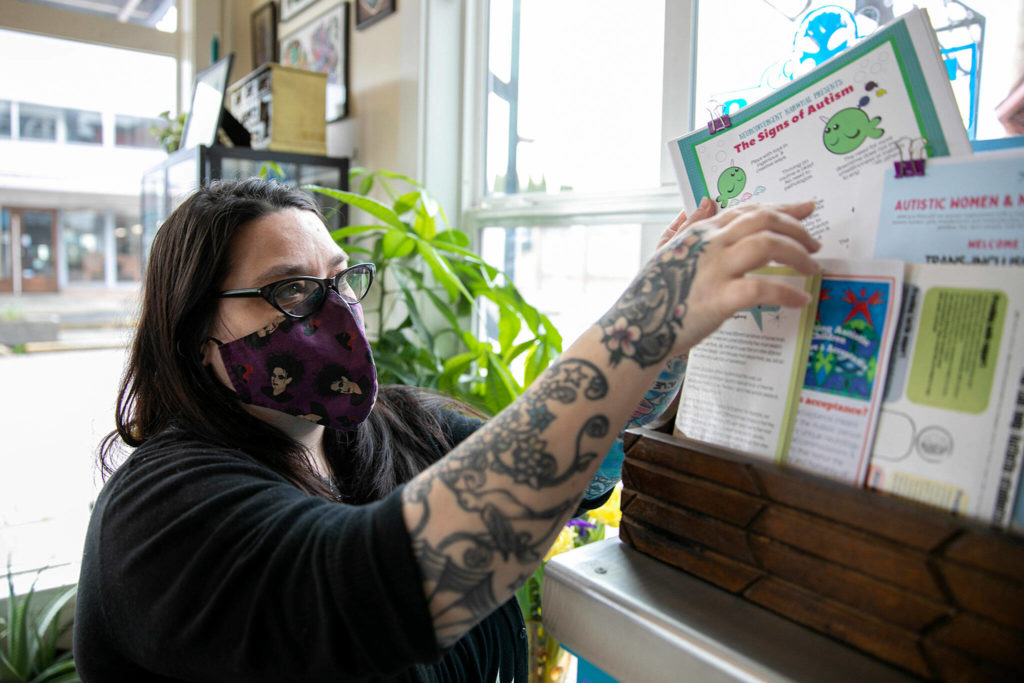 Lei Wiley-Mydske, co-owner of Stanwood Tattoo Company, thumbs through a collection of informational material she has at the autism acceptance library. (Ryan Berry / The Herald)
