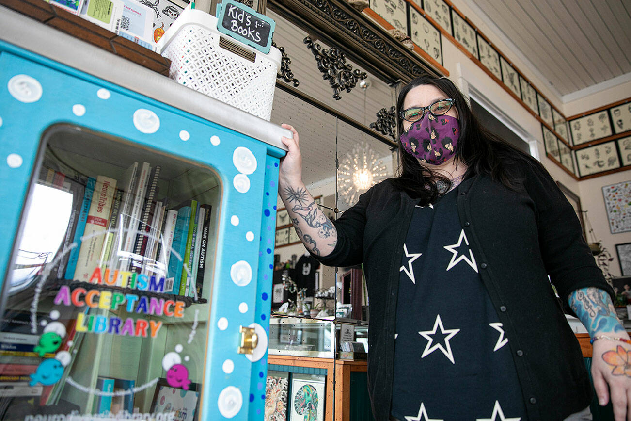 Lei Wiley-Mydske, co-owner of Stanwood Tattoo Company, stands with the Autism Acceptance Library that is installed at her shop on Friday, March 25, 2022, in Stanwood, Washington. (Ryan Berry / The Herald)