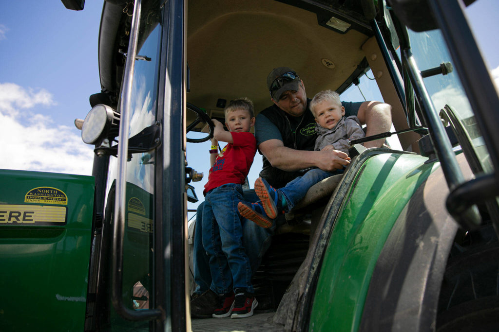 Andrew Albert buckles in his sons Thomas, 2 (right), and Reece, 4, before heading out to fertilize a field across town Friday in Arlington. (Ryan Berry / The Herald)
