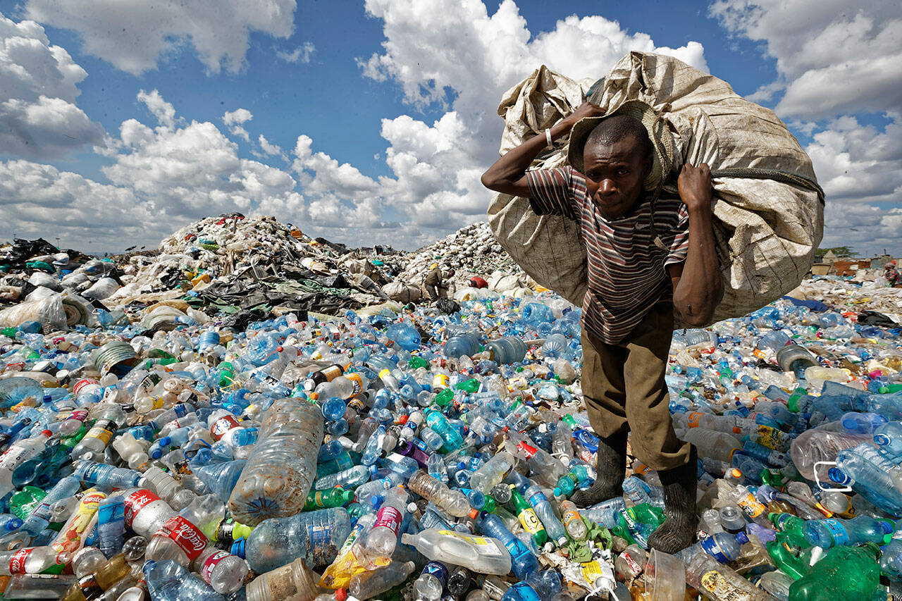 A man walks on a mountain of plastic bottles as he carries a sack of them to be sold for recycling after weighing them at the dump in the Dandora slum of Nairobi, Kenya on Dec. 5, 2018. (Ben Curtis / Associated Press file photo)