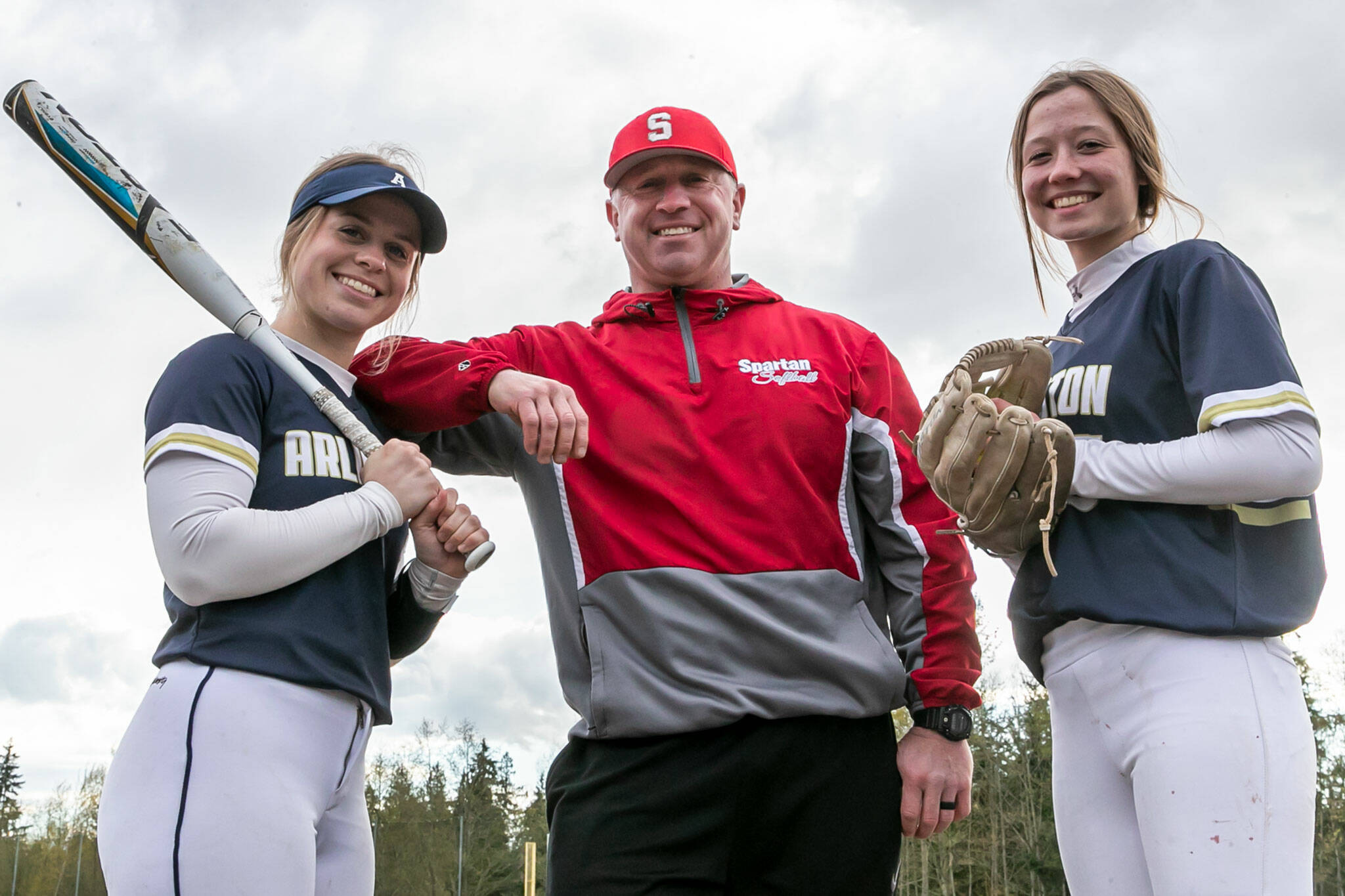 Arlington’s Riley Ryan (left) and Reagan Ryan (right) with their father, Stanwood head softball coach Patrick Ryan. (Kevin Clark / The Herald)