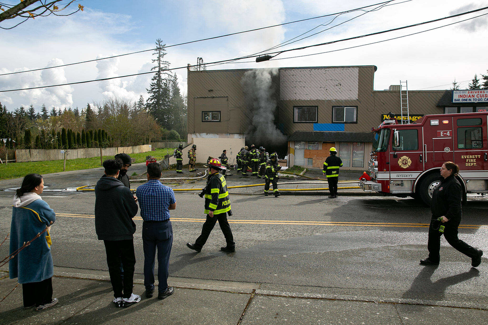 Employees from 5 Rivers Indian Cuisine and other businesses at 9629 Evergreen Way watch as smoke billows out of a lower level garage at the strip mall on Thursday in Everett. (Ryan Berry / The Herald)