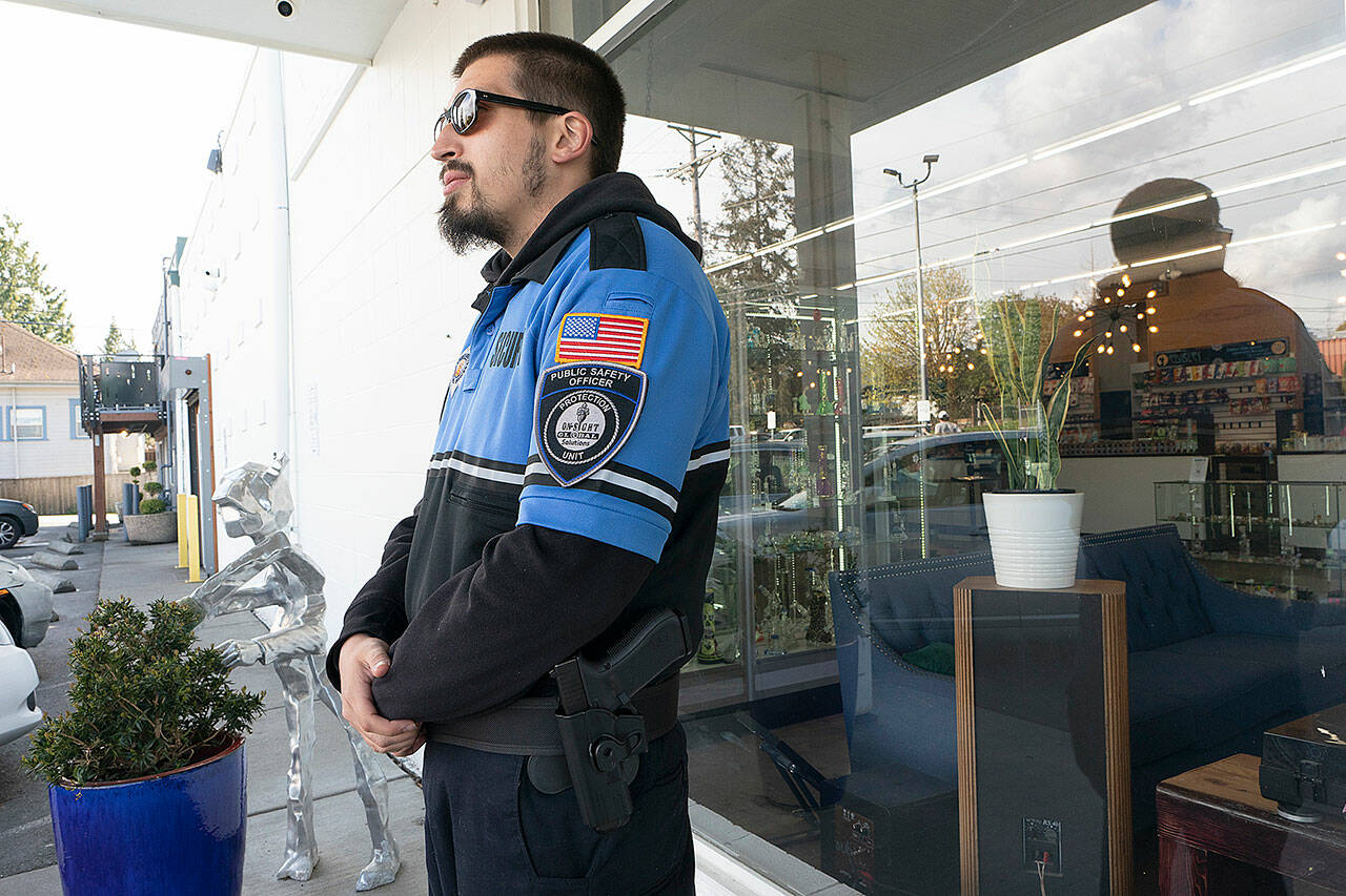 With a gun on his belt, security guard Austin MacMath stands watch outside Mary Mart, a marijuana store in Tacoma. A surge in robberies at licensed cannabis shops in Washington is helping fuel a renewed push for federal banking reforms that would make the cash-dependent stores a less appealing target. (Ted S. Warren / Associated Press)