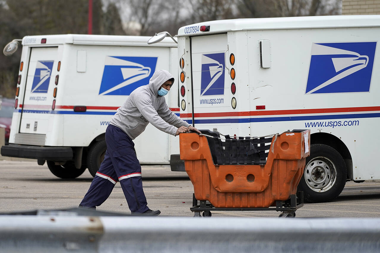 A United States Postal Service employee works outside a post office in Wheeling, Illinois on Dec. 3, 2021. Four environmental groups that want the U.S. Postal Service to buy more electric delivery vehicles are suing to halt further purchases. (AP Photo/Nam Y. Huh, File)