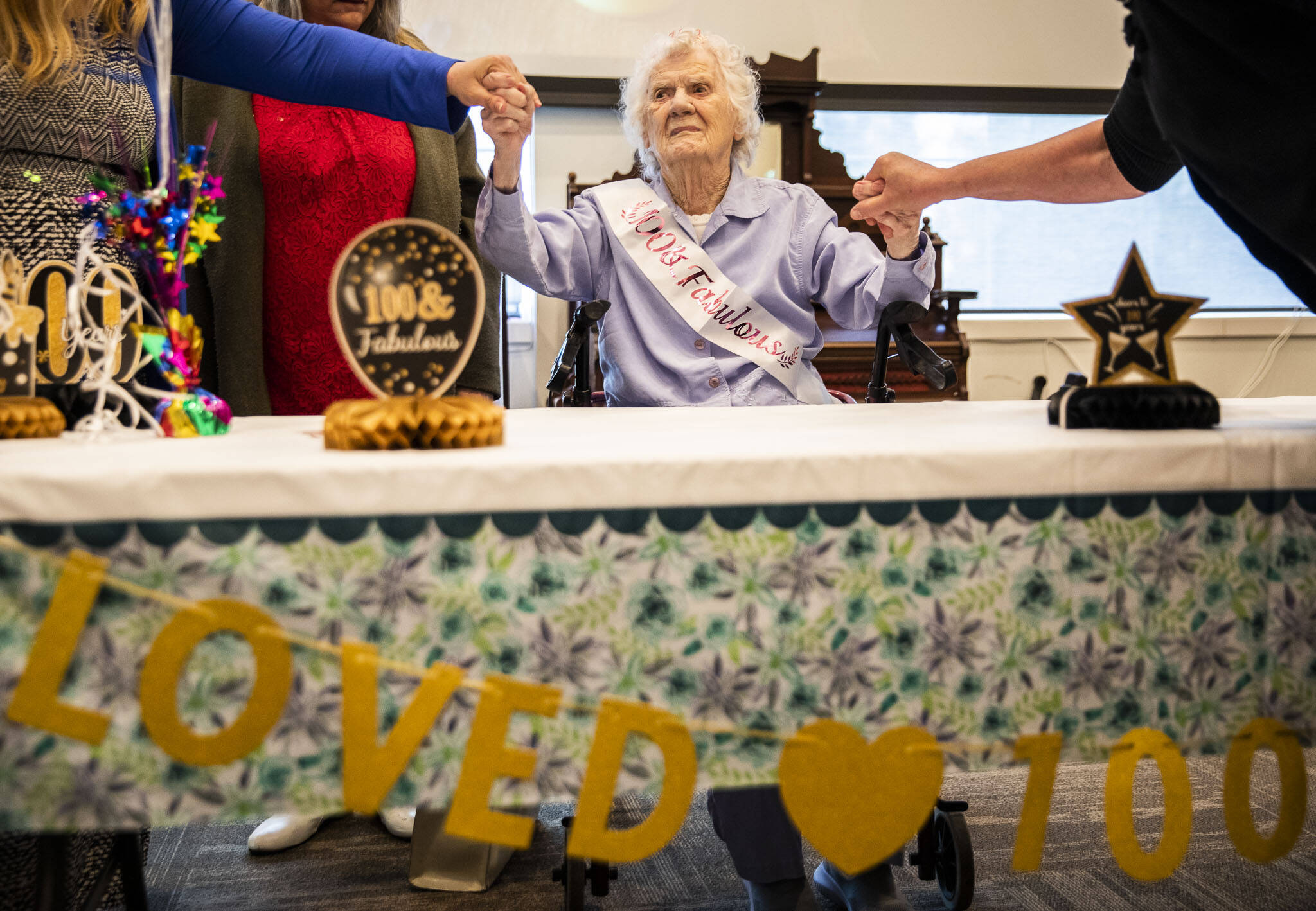 From her seat of honor, Ferne Ullestad holds family members’ hands during her 100th birthday celebration Saturday. (Olivia Vanni / The Herald)