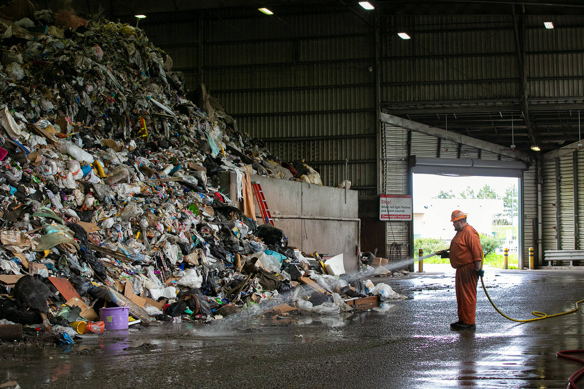 A worker sprays down the floor near a gigantic pile of garbage Friday, April 29, 2022, at the Airport Road Recycling and Transfer Station in Everett, Washington. The garbage pile at the facility is reaching never-before-seen proportions. (Ryan Berry / The Herald)