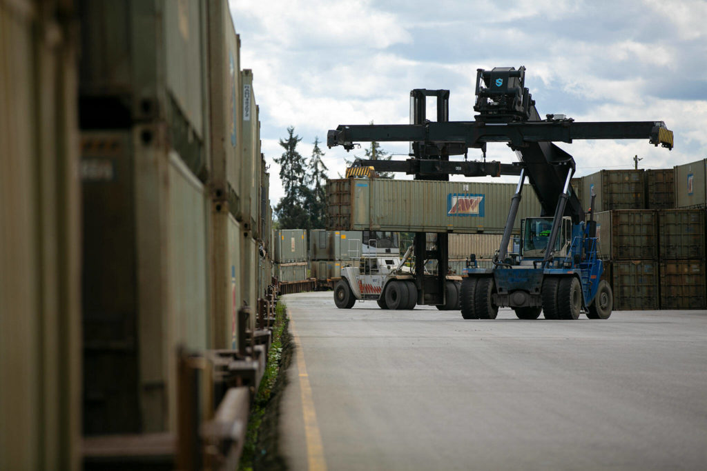 Two machines move bins filled with county trash around a shipping yard Friday along the Snohomish River in Everett. Hundreds of the bins, all filled to the brim, are sitting in the yard awaiting transport via rail. (Ryan Berry / The Herald)
