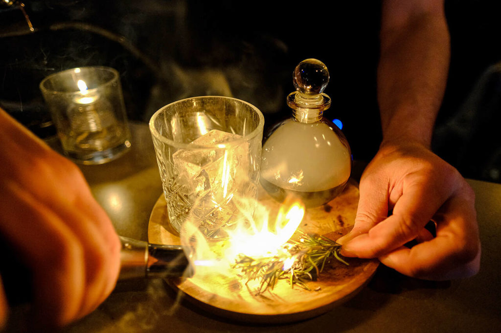 LJ’s Bistro bar manager Andrew Greulich lights up rosemary for some smoky cocktail magic. (Taylor Goebel / The Herald)
