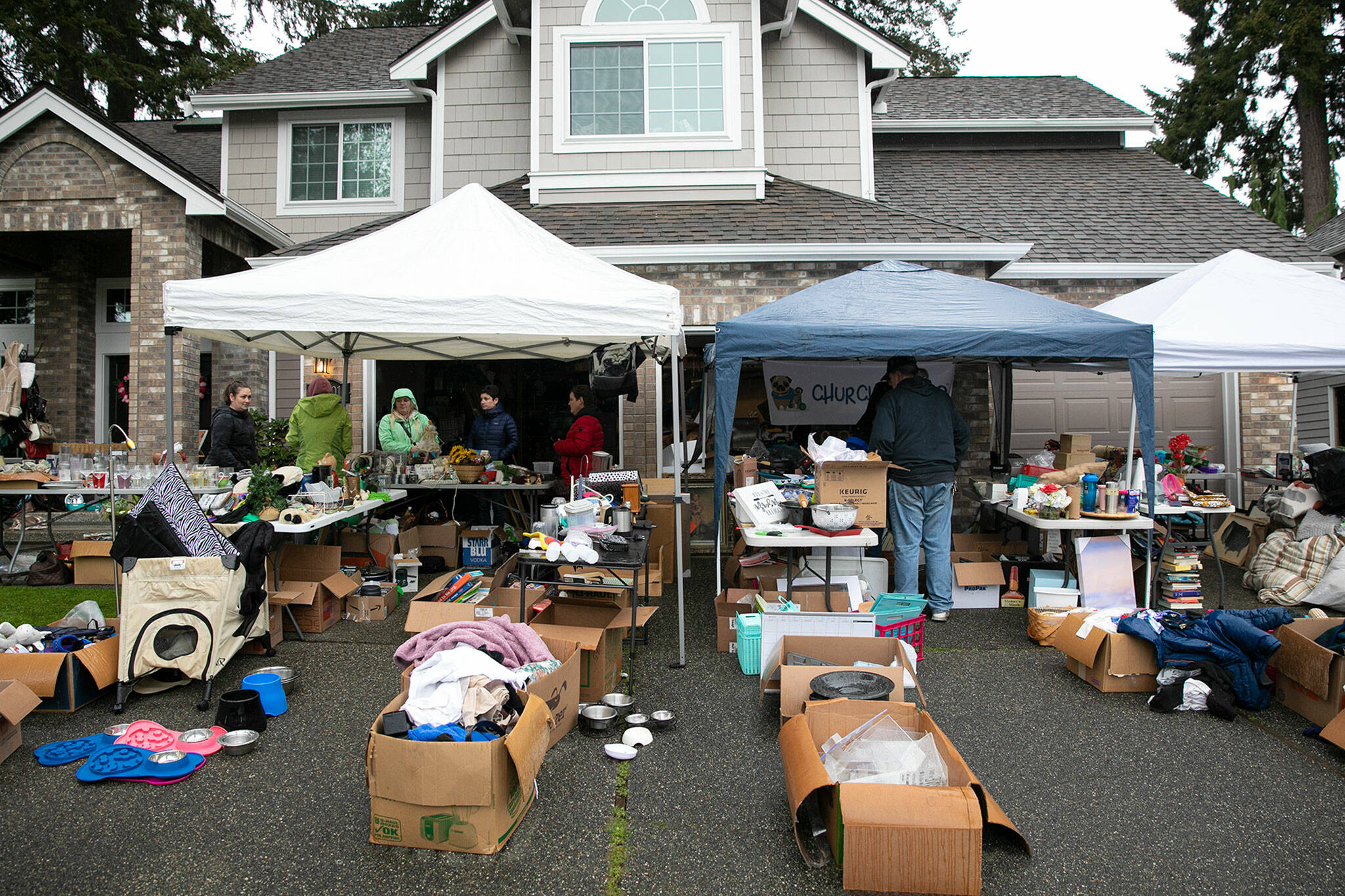 People look around at the non-profit group Church of Pugճ garage sale during the semi-annual Mill Creek community garage sale Saturday in Mill Creek. Many people braved the heavy rain to venture from sale to sale. (Ryan Berry / The Herald)