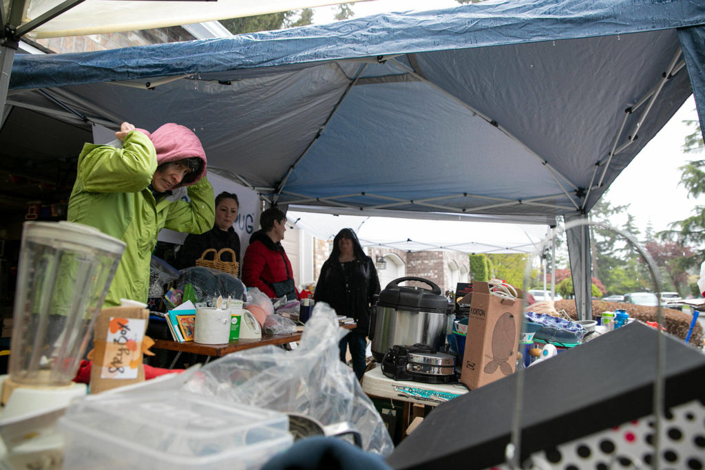 Volunteers from the non-profit group Church of Pug seek shelter from the rain while awaiting customers at a donation-based garage sale Saturday in Mill Creek. The group, which focuses its efforts on providing care for pugs and other dogs in need, hosts a sale at volunteer Heather Campbell’s home during the semi-annual Mill Creek community garage sale. (Ryan Berry / The Herald)
