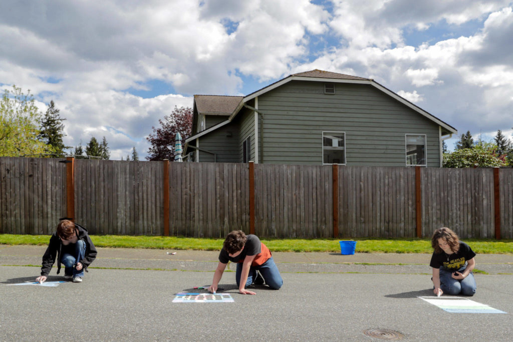 Mia Shields, Sam Bowles and Rhyanna Mercer produce chalk drawings to be washed away by a bucket of water for TikTok videos. (Kevin Clark / The Herald)

