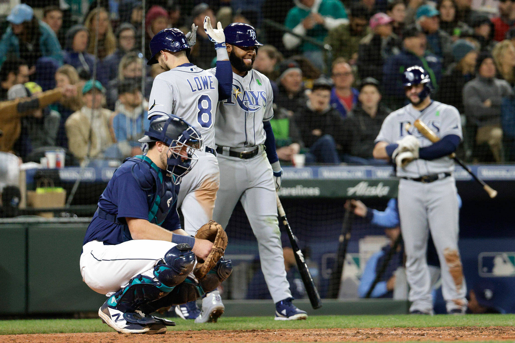 The Rays’ Brandon Lowe (8) celebrates with Manuel Margot at home plate after hitting a home run as Mariners catcher Cal Raleigh looks on during the sixth inning of a game Saturday in Seattle. (AP Photo/Jason Redmond)