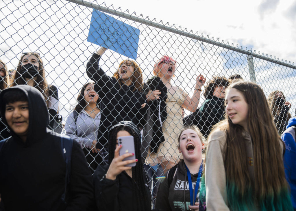 North Middle School eighth graders Cynthia Espinoza (left) and Fern Conroy (right) chant with Everett High School students from the other side of a perimeter fence surrounding the middle school on Monday. (Olivia Vanni / The Herald)
