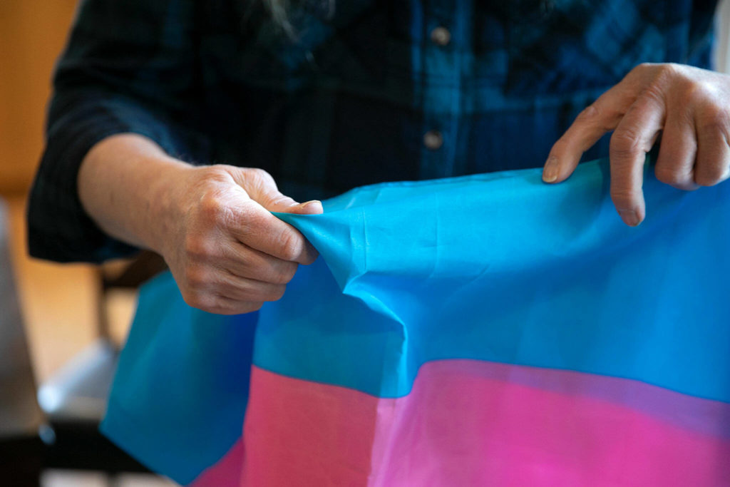 Melissa Batson holds the transgender flag while rifling through the different flags she owns at her home in Monroe. Batson is a transgender woman and flies the flag every Nov. 20 — the Transgender Day of Remembrance — to honor transgender people who have lost their lives to transphobic violence. (Ryan Berry / The Herald)
