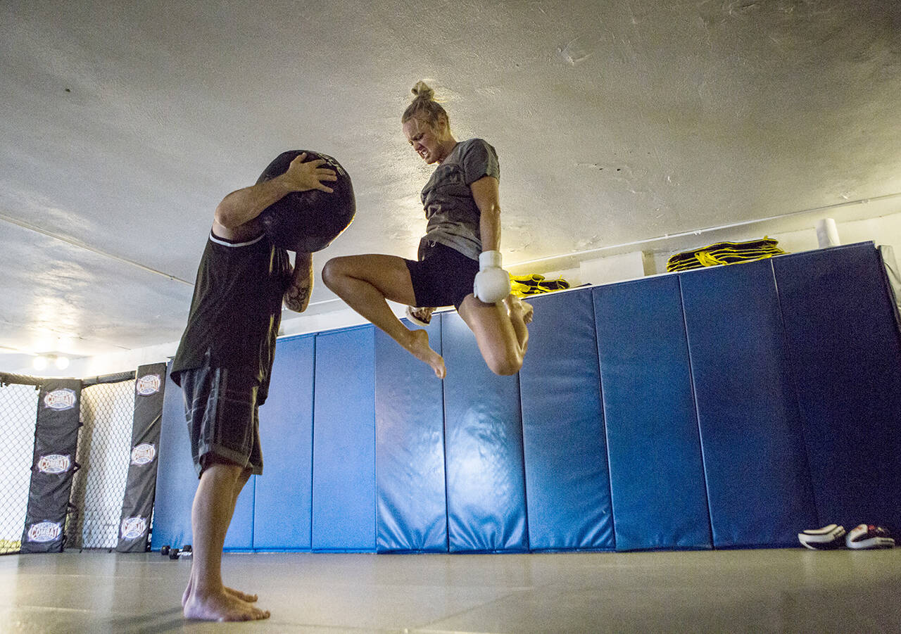 Miranda Granger jumps in the air to knee a medicine ball being held by Charlie Pearson during her training session at Charlie’s Combat Club on Friday, July 26, 2019, in Everett. (Olivia Vanni / The Herald)