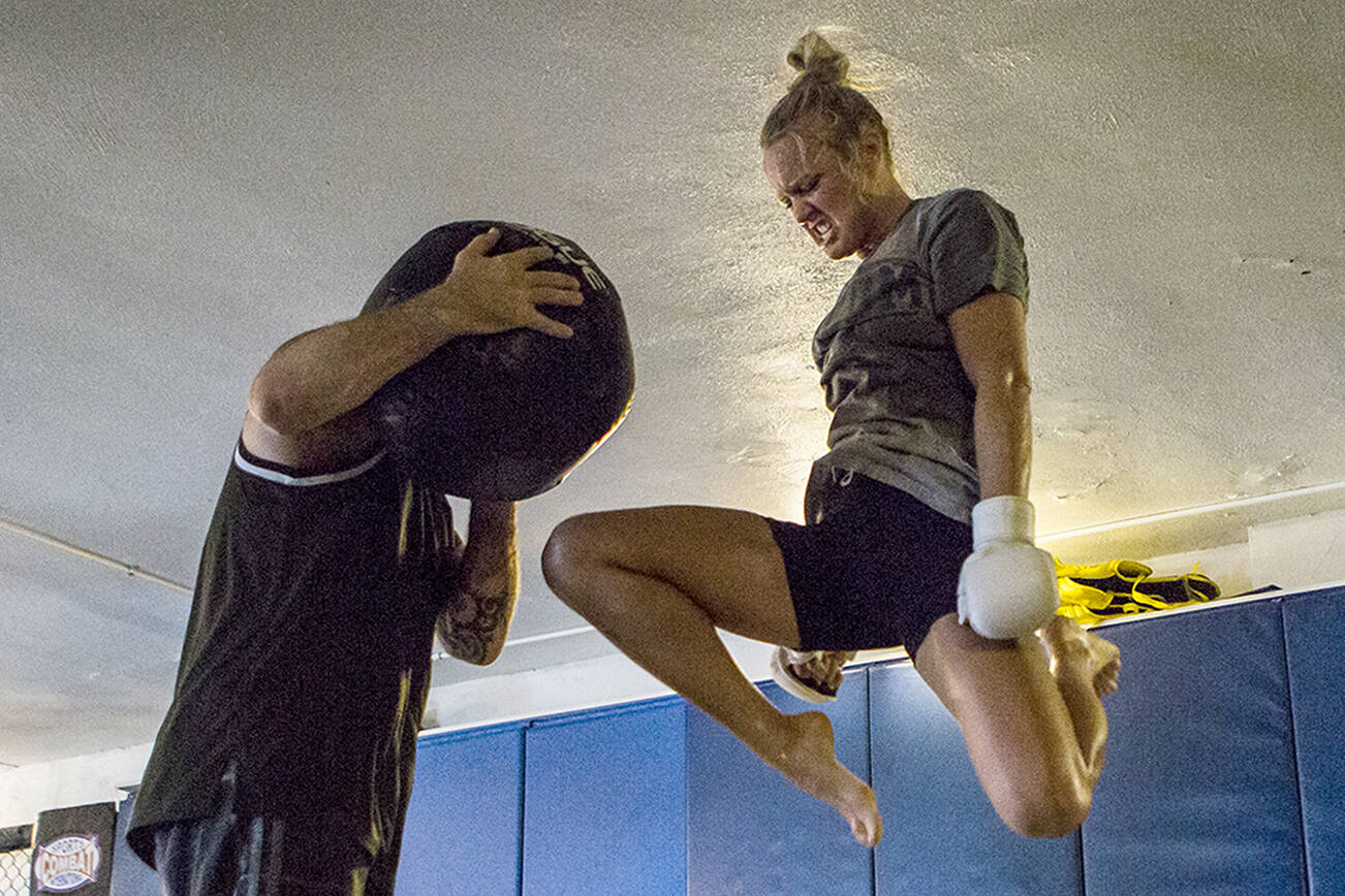 Miranda Granger jumps in the air to knee a medicine ball being held by Charlie Pearson during her training session at Charlie's Combat Club on Friday, July 26, 2019 in Everett, Wash. (Olivia Vanni / The Herald)