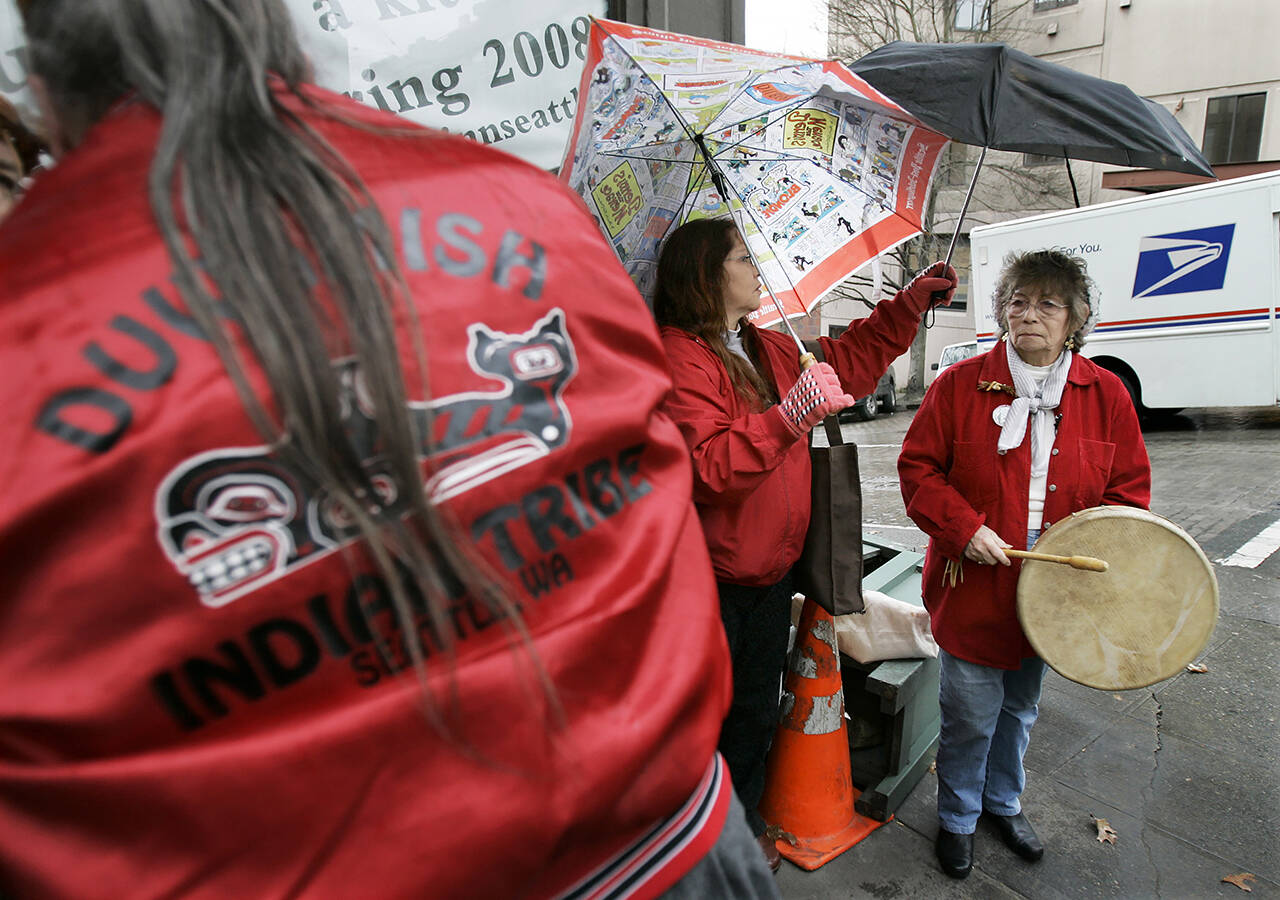 Barbara Williams (center) holds an umbrella for her mother, tribal chair Cecile Hansen (right), as they prepare to join other members of the Duwamish Indian Tribe in performing an “honor song” in 2008 near a location in Seattle where bones were found during construction activities near the Pike Place Market. (AP Photo/Ted S. Warren, file)