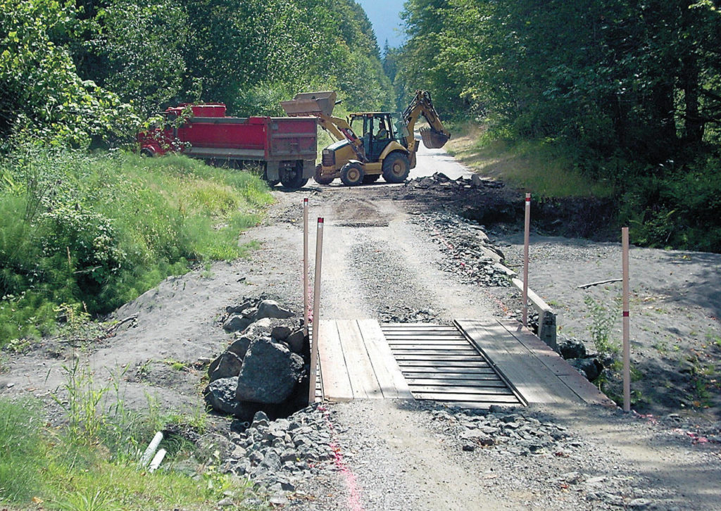 An excavator loads pieces of old roadway into a dump truck at the site of a washout on Olympic Hot Springs Road in the Elwha Valley of Olympic National Park in 2016. (Keith Thorpe / Peninsula Daily News file)
