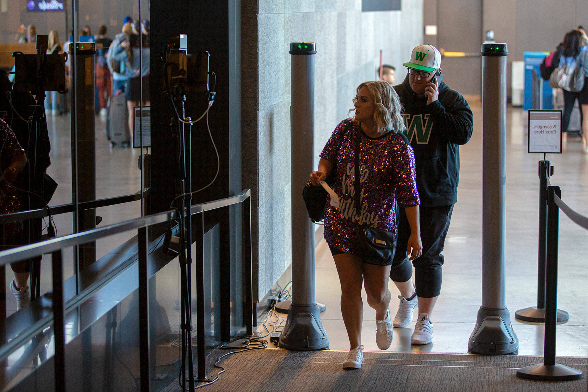 Two travelers walk through two pillars of an Athena screening device on Friday, May 27, 2022, at Paine Field in Everett, Washington. The device works like a metal detector and helps identify weapons on people preparing to go through TSA. (Ryan Berry / The Herald)