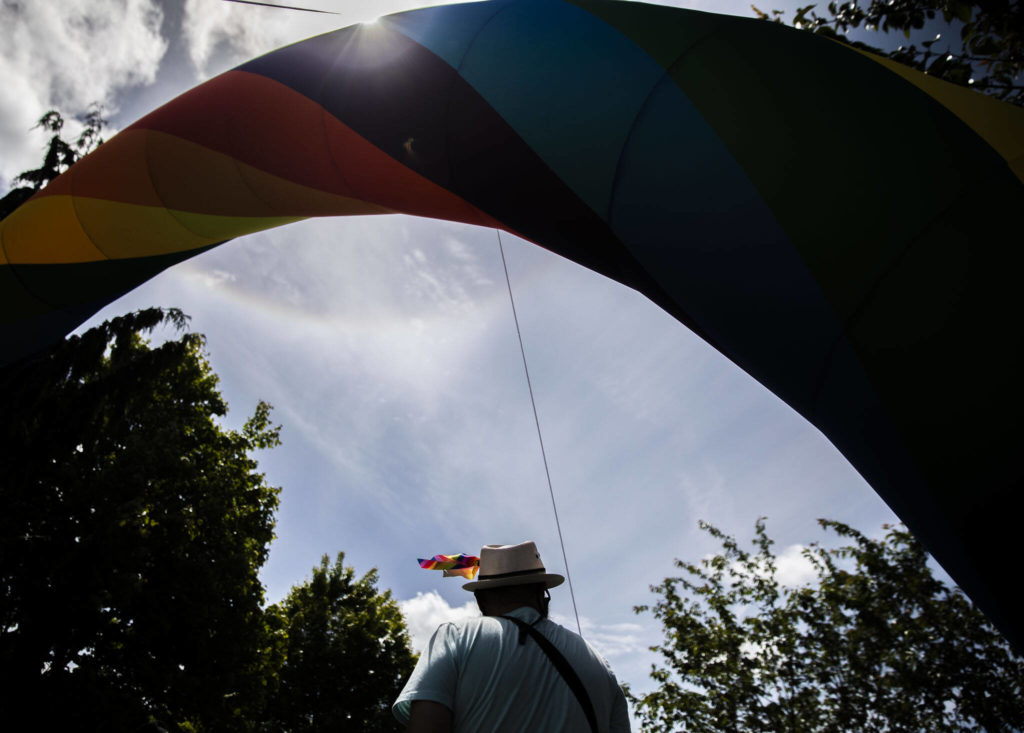 A person wearing a small rainbow flag on their hat passes under a rainbow arch at Arlington’s first-ever Pride celebration Saturday. (Olivia Vanni / The Herald)
