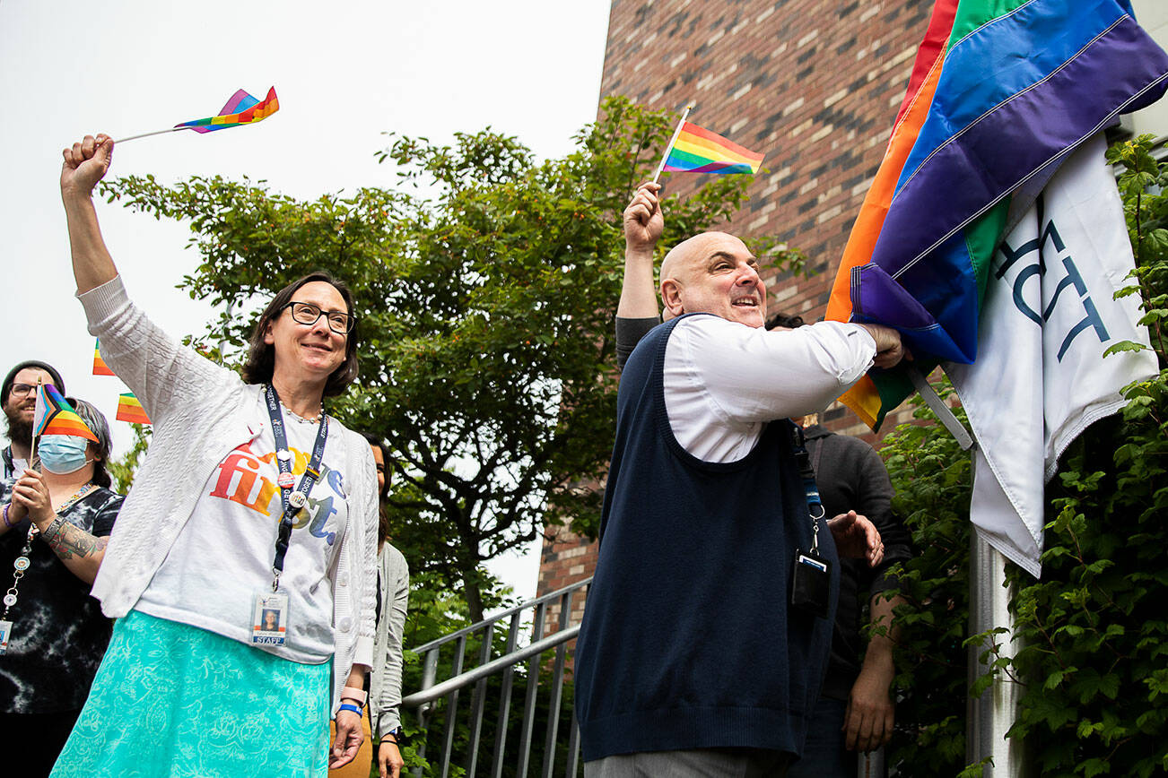 Laura Phillips, left, waves a rainbow flag while Everett Public Schools superintendent Ian Saltzman raises a PRIDE rainbow flag at the Everett Public School’s PRIDE month celebration on Wednesday, June 1, 2022 in Everett, Washington. (Olivia Vanni / The Herald)