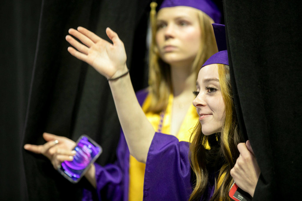 Students peek through the stage curtain to find family before Lake Stevens High School’s 2022 commencement ceremony Tuesday at Angel of the Winds Arena in Everett. (Ryan Berry / The Herald)
