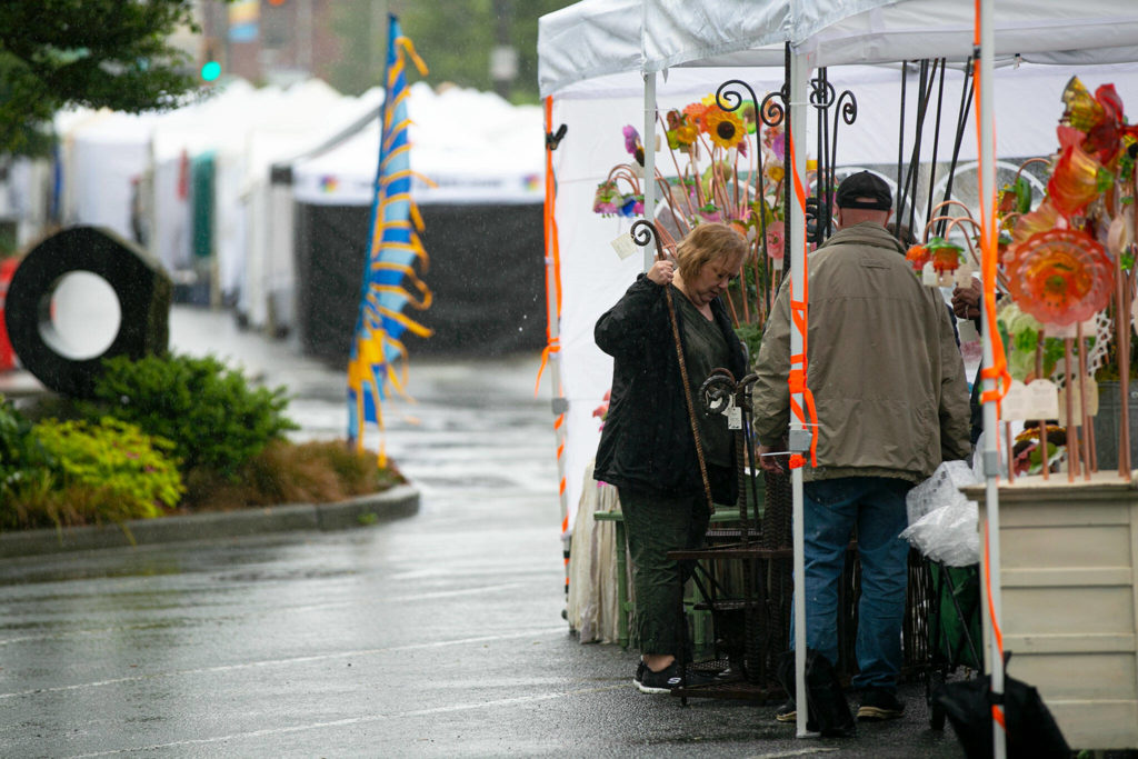 Suzanne Quirk and the rest of the crew from Lake Forest Park’s Vintage Glass Gardens work under their canopy during steady rain as vendors prepare for the Sorticulture Garden Arts Festival Thursday in downtown Everett. (Ryan Berry / The Herald) 
