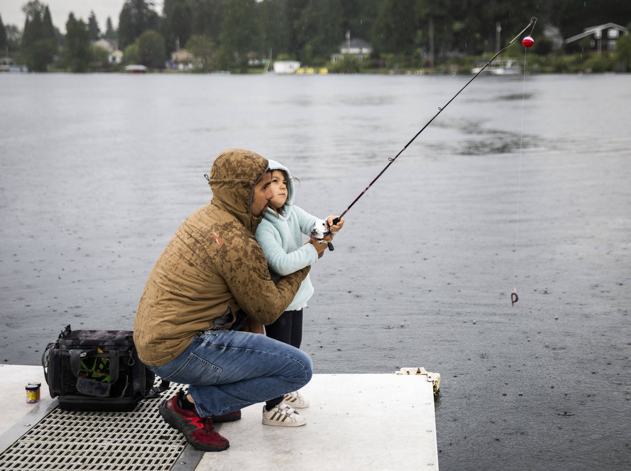 Ridley Biggs (right), 5, learns how to cast with her father, Mike Biggs, as it starts to rain on Friday in Lake Stevens. (Olivia Vanni / The Herald)