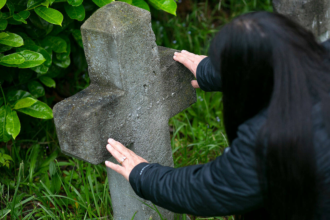 Candy Hill-Wells, funeral services officer for the Tulalip Tribes, tries to read the weathered letters on a grave marker Tuesday, June 14, 2022, at Priest Point Cemetery in Tulalip, Washington. (Ryan Berry / The Herald)