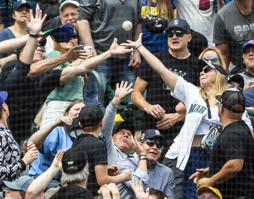 Spectators all reach out to catch a foul ball during the game against the Angels on Sunday, June 19, 2022 in Seattle, Washington. (Olivia Vanni / The Herald)

