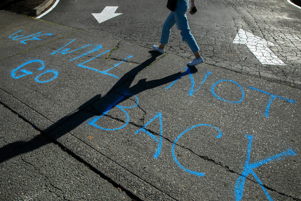 A woman walks past writing saying, “We will not go back,” during a protest against the Supreme Court’s decision to overturn Roe v. Wade on Friday along Broadway in Everett, Washington. (Ryan Berry / The Herald)
