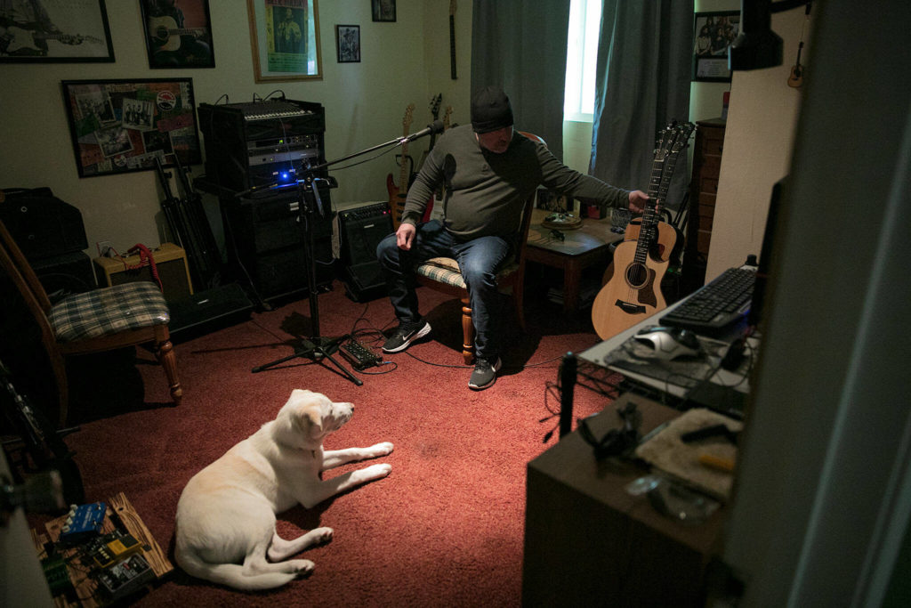 Nik Clovsky reaches for his guitar as his dog, Bo Diddley, relaxes. (Ryan Berry / The Herald)
