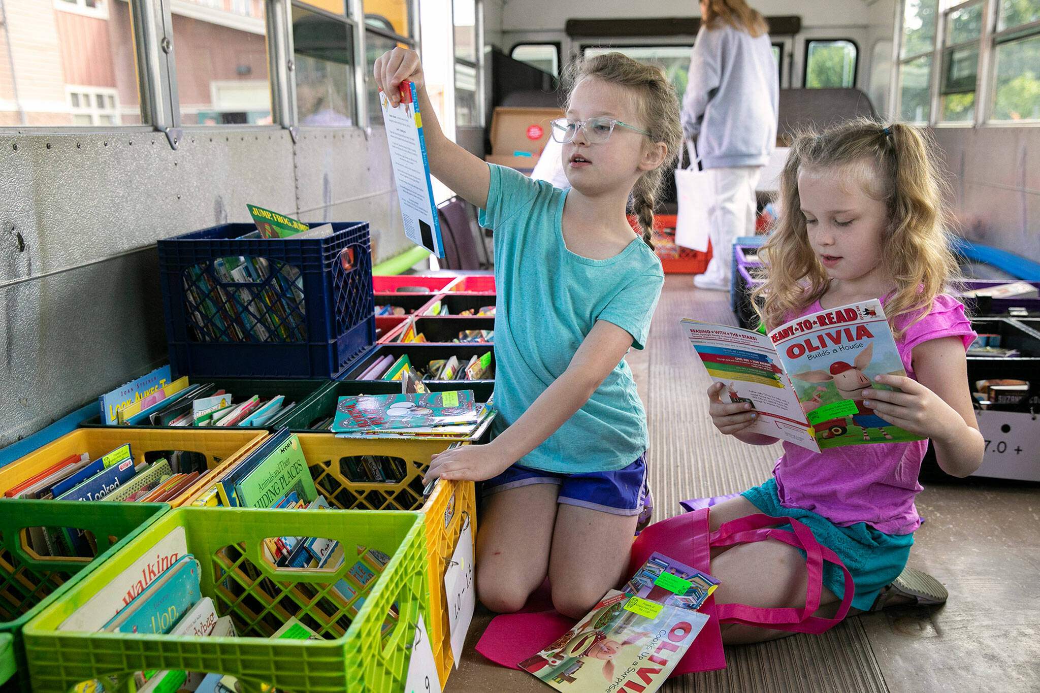 Second-grade twins Emily and Alison Johnson take a look through books available in their reading range while spending time at the Arlington School District’s Cool Bus on July 6, at Presidents Elementary School in Arlington. (Ryan Berry / The Herald)