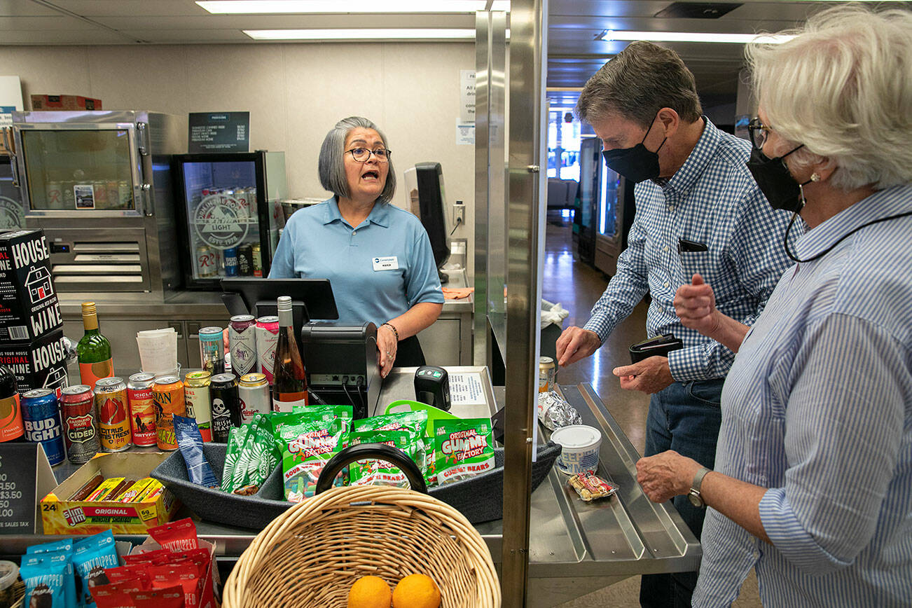 Maria Rios, a ferry worker of 13 years, helps Frank and Fran Butler, both of Washington, D.C., check out as the couple purchases food on Thursday, July 21, 2022, aboard the MV Suquamish ferry between Mukilteo and Clinton, Washington. Rios said food service returned to the Suquamish about three weeks prior. (Ryan Berry / The Herald)