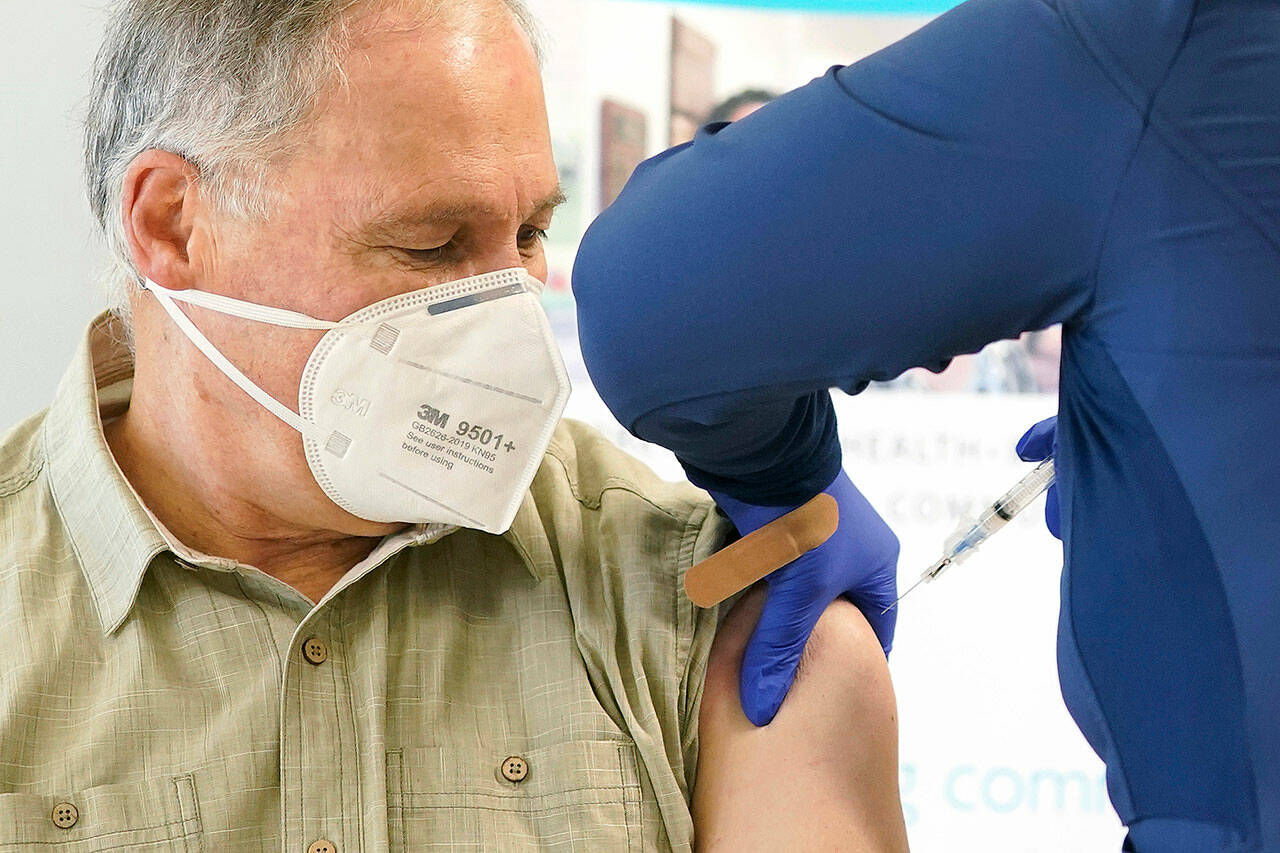 Gov. Jay Inslee, left, gets the first shot of the Moderna COVID-19 vaccine, Jan. 22, 2021, from Elizabeth Smalley, right, a medical assistant at a Sea Mar Community Health Center in Olympia. (AP Photo/Ted S. Warren)