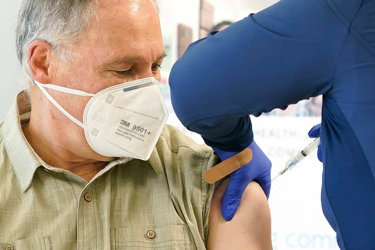 Washington Gov. Jay Inslee, left, gets the first shot of the Moderna COVID-19 vaccine, Friday, Jan. 22, 2021, from Elizabeth Smalley, right, a medical assistant at a Sea Mar Community Health Center in Olympia, Wash. Inslee's wife Trudi also received the first dose of the vaccine. (AP Photo/Ted S. Warren)