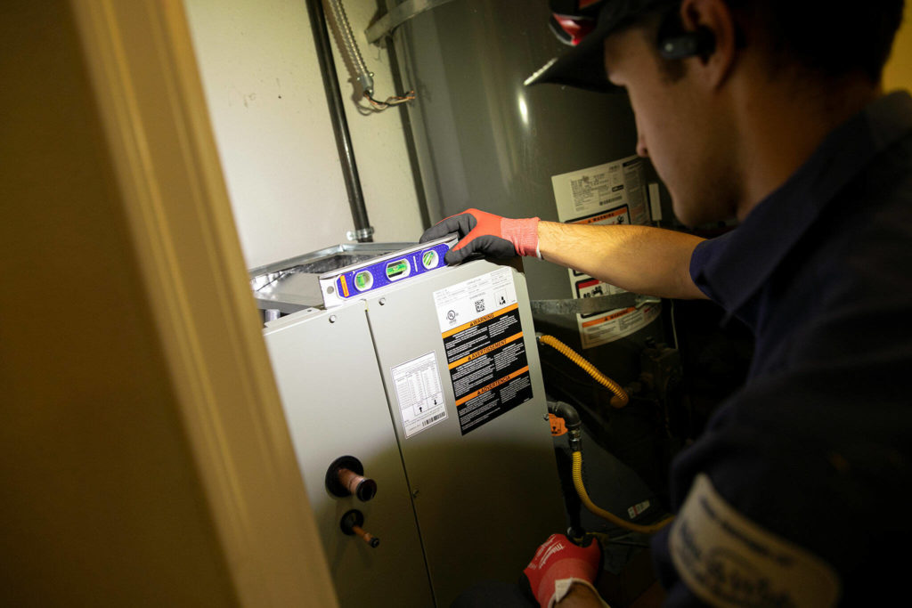 Trent Pickford, a lead installer with CM Heating, makes sure a new HVAC coil is level before fastening it in place Friday, at a home in Woodinville. The coil is capable of pumping both hot and cool air through a home’s ductwork. (Ryan Berry / The Herald) 
