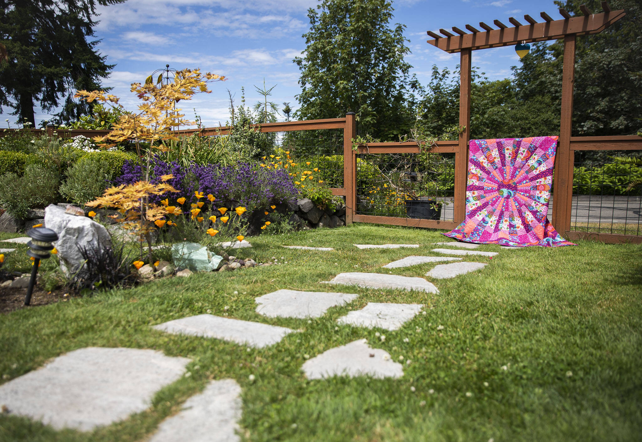 A quilt titled “Wheel of Fortune” hangs on the fence at the Mukilteo Garden Quilt Tour home of gardeners MaryJane Cavanagh and Les Nelson. The tour is July 16 and 17. (Olivia Vanni / The Herald)