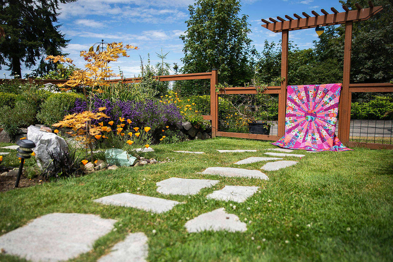 A quilt titled “Wheel of Fortune” hangs on the fence at one of the Mukilteo garden-quilt tour homes on Thursday, July 7, 2022. (Olivia Vanni / The Herald)