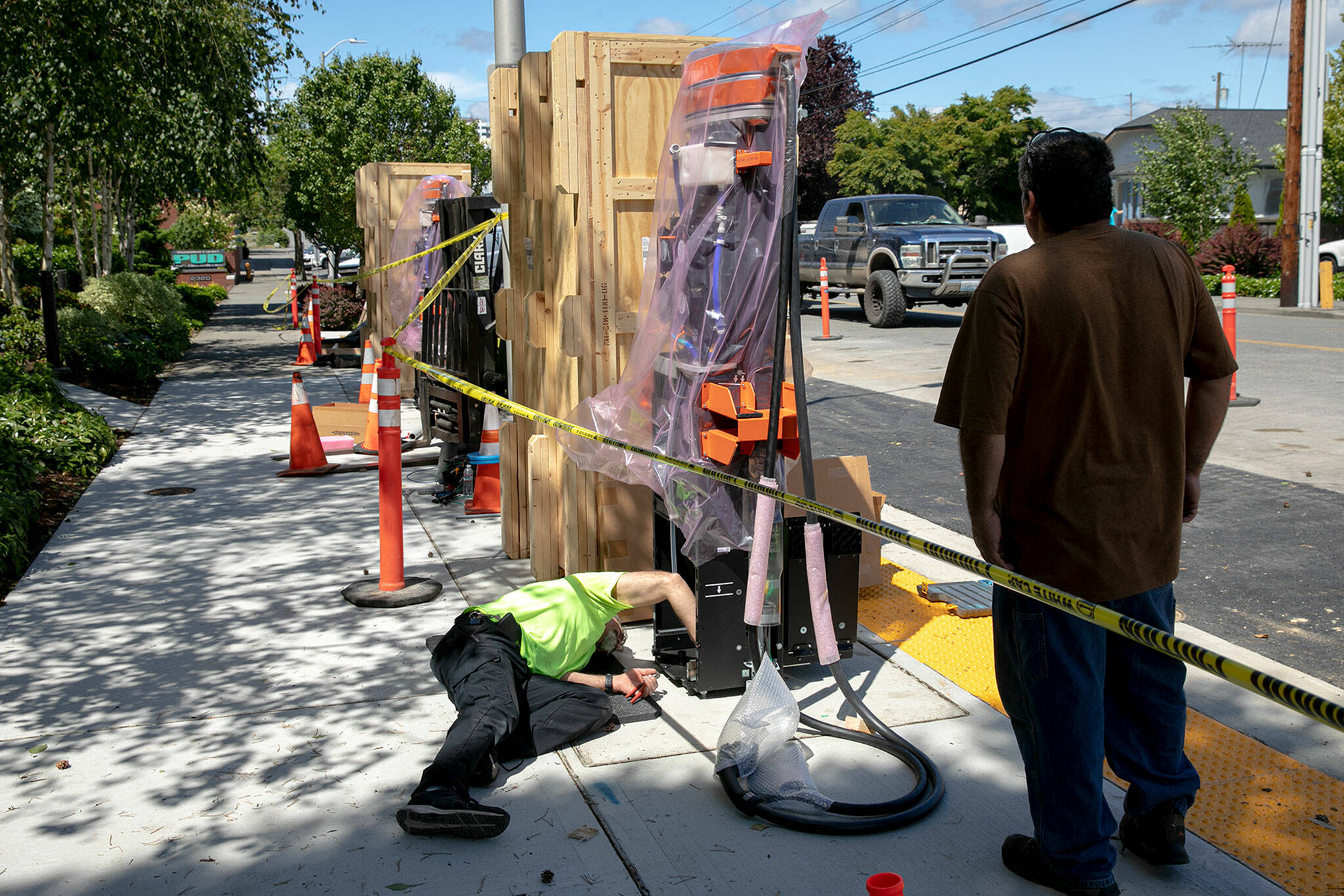 Workers install two new electric vehicle fast charging stations along California Street on June 28 at the Snohomish County PUD headquarters in Everett. (Ryan Berry / The Herald)