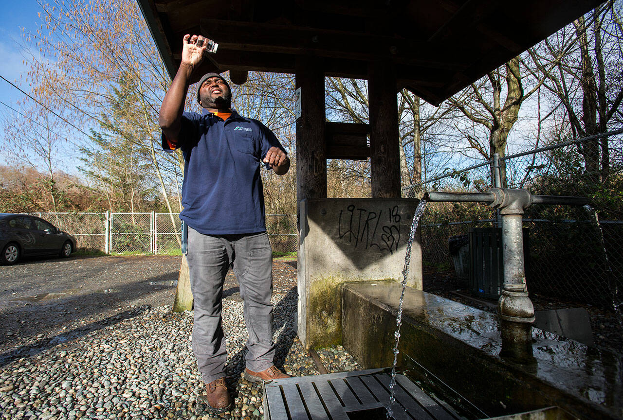 Alderwood Water & Wastewater District water quality tech assistant Matt Williams looks at the clarity of a water sample taken from the artesian well located along164th Street on April 2, 2018 in Lynnwood. (Andy Bronson / The Herald)